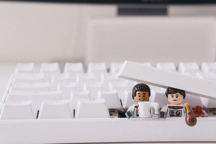 Zwei Lego-Figuren schauen aus einer weißen Tastatur heraus.