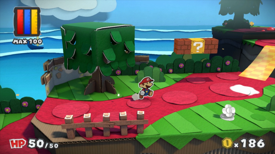 Mario läuft auf einem roten Weg durch eine Welt. Man sieht Bäume, einen kleinen Zaun und Mario-typische ?-Boxen. Alles sieht aus wie aus Pappe gebastelt.